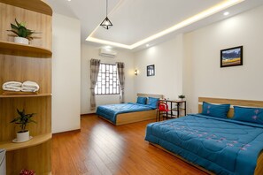 A hotel room with two beds, wooden flooring, a ceiling light fixture, a window with curtains, and a wall-mounted picture.