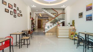 A modern hotel lobby with a staircase, wooden reception desk, and several tables and chairs. - 10 Dollar Homestay Danang - Hostel (Da Nang)