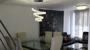 A modern dining area with a glass table, white chairs, and a chandelier. - Pereira-Cerritos Casa (Pereira)