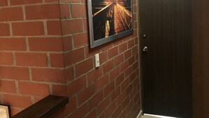 A hallway with a brick wall, a framed picture of a bridge, a wooden door, and a small shelf. - Pereira-Cerritos Casa (Pereira)