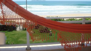 Eine Hängematte auf einem Balkon mit Blick auf einen Strand, Wellen und eine entfernte Insel.