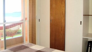 Ein Schlafzimmer mit großem Fenster, einem Bett, einem Kleiderschrank und einem Sessel.