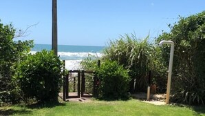 Ein Rasenbereich mit einem Tor, das zu einem Weg führt, umgeben von dichtem Grün und freiem Blick auf das Meer.
