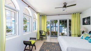 A bedroom with a bed, a chair, a small table, a ceiling fan, and a view of the outdoors through a sliding glass door.