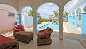 A covered outdoor area with wicker furniture, a pool, and a view of the ocean.
