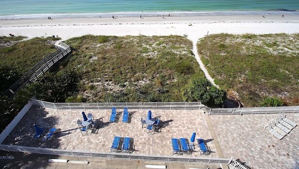 Vista de una playa con un área de patio que incluye sillas de sol y un camino que lleva a la playa.
