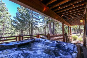 Un bain à remous installé sur une terrasse en bois à l’extérieur, avec vue sur des pins.