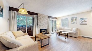 Een woonkamer met een bank, salontafel, open haard en grote ramen.