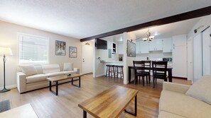 Een moderne woonkamer met een bank, salontafel en een eethoek met stoelen, met een keuken op de achtergrond.