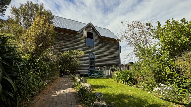 A rustic wooden house with a sloped roof, a front porch, and a pathway leading to the entrance. - NOT JUST A STAY,  we are a stay you will remember! (Kaikoura Township)