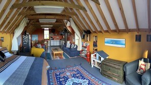 An attic-style room with a high ceiling, wooden beams, a bed, a sofa, a small table, a bookshelf, and a painting on the wall. - NOT JUST A STAY,  we are a stay you will remember! (Kaikoura Township)