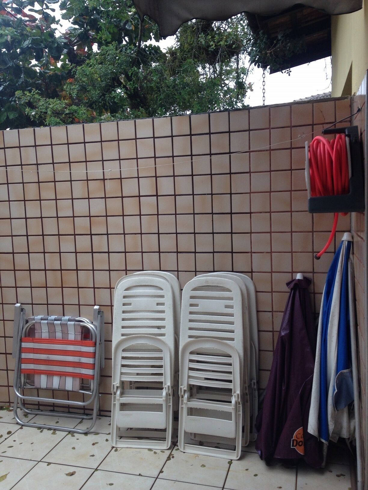 A tiled wall with two white plastic chairs and a metal chair leaning against it.