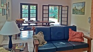 A cozy living room with a blue sofa, a table with a lamp, and a view of the outdoors through large windows.