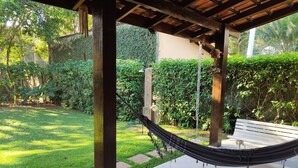 A hammock under a wooden pergola in a garden with a bench and lush greenery.