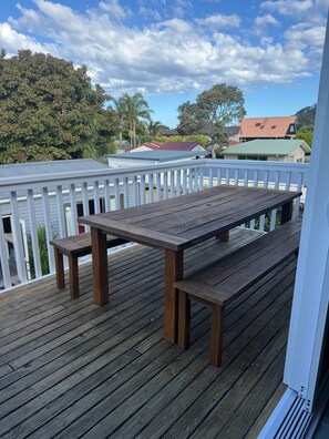 Un patio in legno con tavolo e panche, circondato da un parapetto bianco.