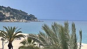 Eine Küstenlandschaft mit Strand, Palmen und einer Burg auf einem Hügel.