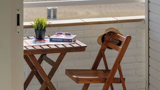 Ein Balkon mit Holzstuhl und Tisch, einer Topfpflanze und einer Sonnenbrille.