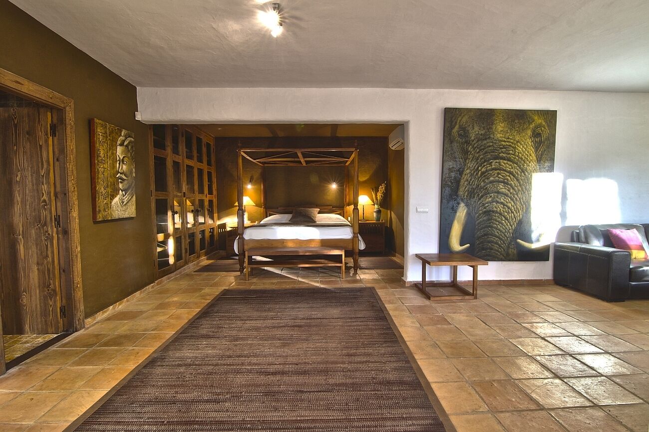 Een slaapkamer met een bed, bedlampjes, een groot schilderij van een olifant en een houten deur.