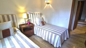 A hotel room with two beds, a nightstand with a lamp and a potted plant, and a wall-mounted light fixture.