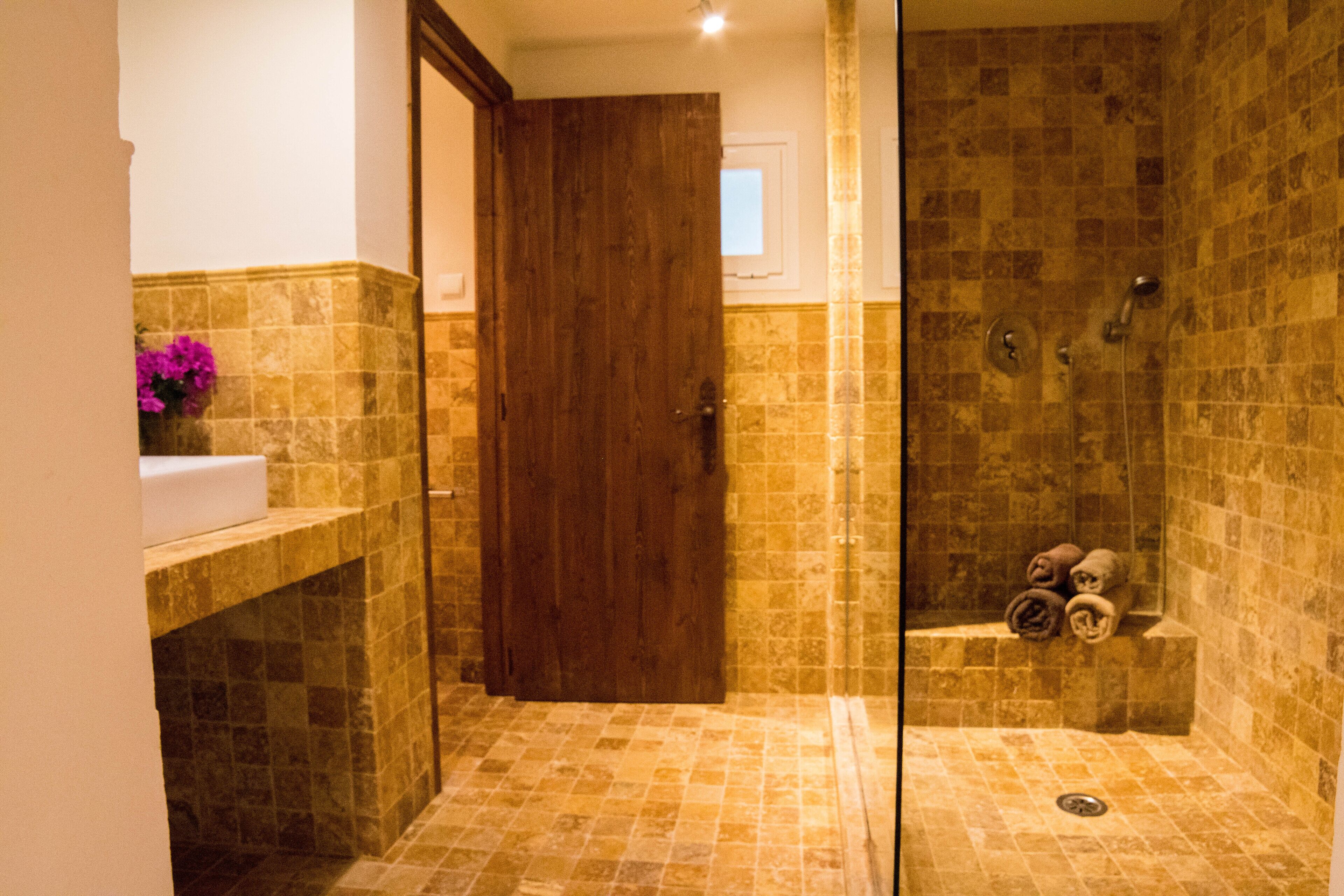 Ein Badezimmer mit Holztür, Waschbecken und Duschbereich mit gefliesten Wänden und Boden.