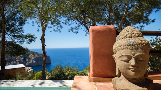 A stone Buddha statue by a pool with a view of the sea.