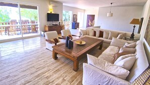 A spacious living room with a wooden coffee table, white sofas, and a television on a wooden cabinet.