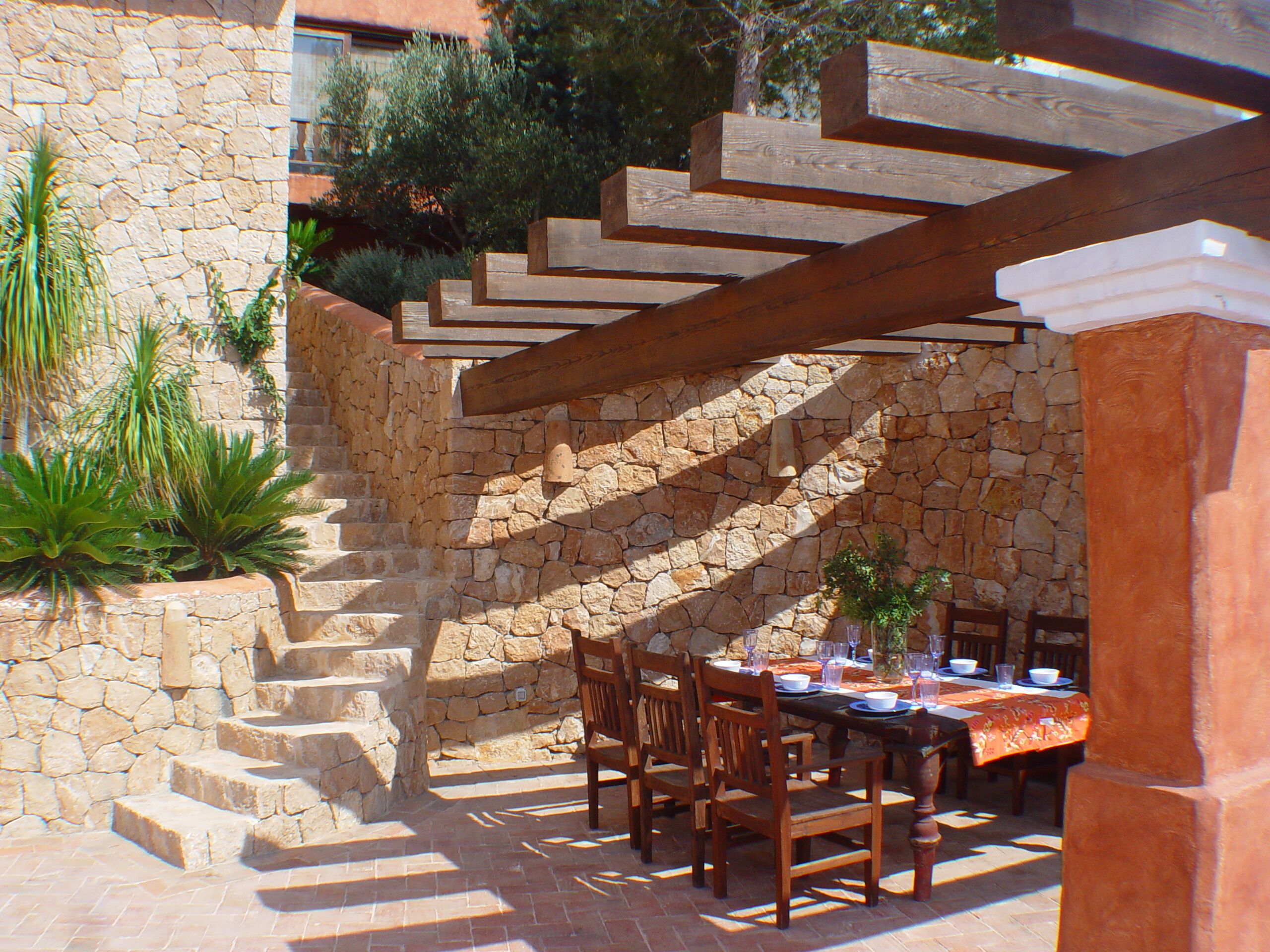 A stone staircase leading to a covered outdoor dining area with wooden chairs and a table set for dining.
