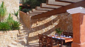 A stone staircase leading to a covered outdoor dining area with wooden chairs and a table set for dining.