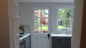 A narrow kitchen with a white door, a window, and a view of a garden. - Pearl River Cottage in South Devon (Kingsbridge)