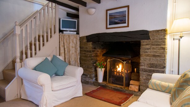 A living room with a fireplace, a white sofa, a television on a shelf, and a staircase. - Pearl River Cottage in South Devon (Kingsbridge)