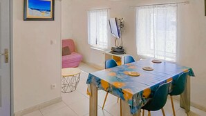 Un coin repas avec une table recouverte d’une nappe colorée, des chaises bleues et un canapé rose en arrière-plan.