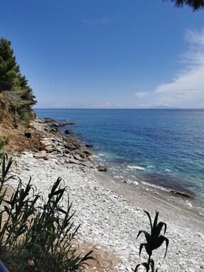 A rocky beach with clear blue water and distant mountains.