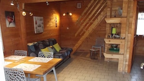 L’intérieur d’un chalet en bois chaleureux et accueillant, avec un coin repas, un canapé et un escalier.