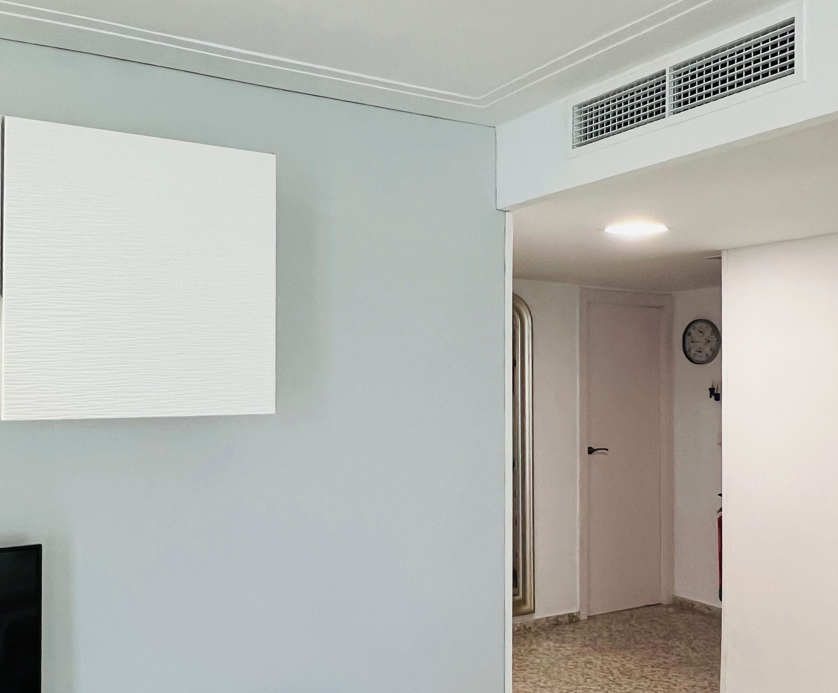 A room with a white wall, a door leading to another room, and a ceiling vent.
