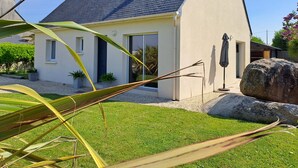 Een modern huis met een schuin dak, een klein voortuintje en een grote rots in de voortuin.