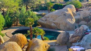 Un área de piscina con rocas grandes, palmeras y una pérgola.