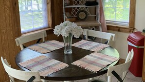 A round dining table with white chairs, a vase with white flowers, and striped placemats.