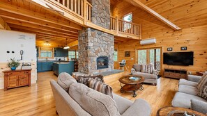 A spacious living area with a stone fireplace, wooden ceiling beams, and a television.