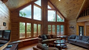 Un salon spacieux doté de grandes fenêtres, de murs en bois et d’un plafond haut.