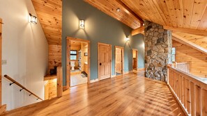 A spacious interior with a wooden staircase, a stone accent wall, and a view into a bathroom. - Grand Ebs View Lodge, Luxury Log Home, Views, Hot Tub, Sauna, EV Charge, 3D Tour (Jay)