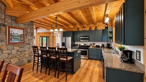 A kitchen with wooden beams, a stone wall, and a bar area with chairs. - Grand Ebs View Lodge, Luxury Log Home, Views, Hot Tub, Sauna, EV Charge, 3D Tour (Jay)