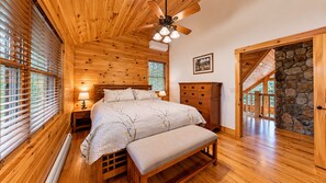 A bedroom with a wooden ceiling, a bed with a white bedspread, a nightstand, a dresser, and a stone wall. - Grand Ebs View Lodge, Luxury Log Home, Views, Hot Tub, Sauna, EV Charge, 3D Tour (Jay)