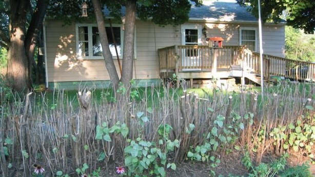 A house with a front porch, a small deck, and a garden with various plants and flowers.