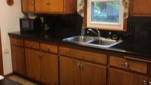 A kitchen with wooden cabinets, a black countertop, a stainless steel sink, and a window with a floral curtain.