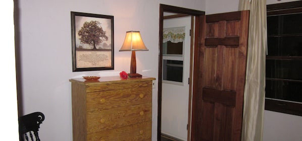 Un aparador de madera con cajones, un cuadro con un árbol y una lámpara de mesa.