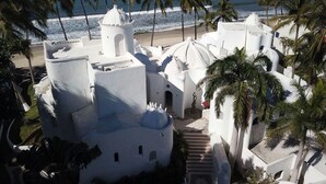 Un edificio blanco con múltiples cúpulas, rodeado de palmeras y una playa.