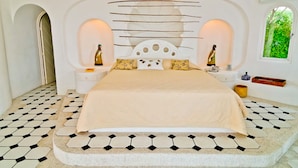 Un dormitorio con una cama grande, dos mesitas de noche, un cabecero decorativo y vistas al verdor a través de una ventana.