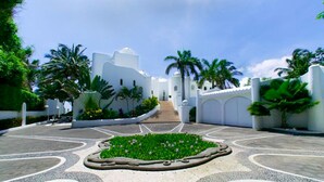 Un patio con jardín central, edificios blancos, palmeras y una escalera que lleva a un nivel superior.