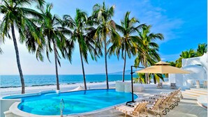 Zona junto a la piscina con vista despejada al océano, rodeada de palmeras y sillones de descanso.