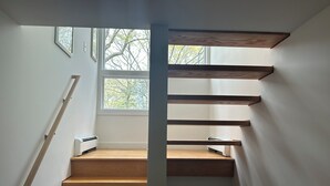 A staircase with wooden steps and a view of trees through a window. - Bright and Spacious Summer Home Steps from the Beach (Shelter Island)
